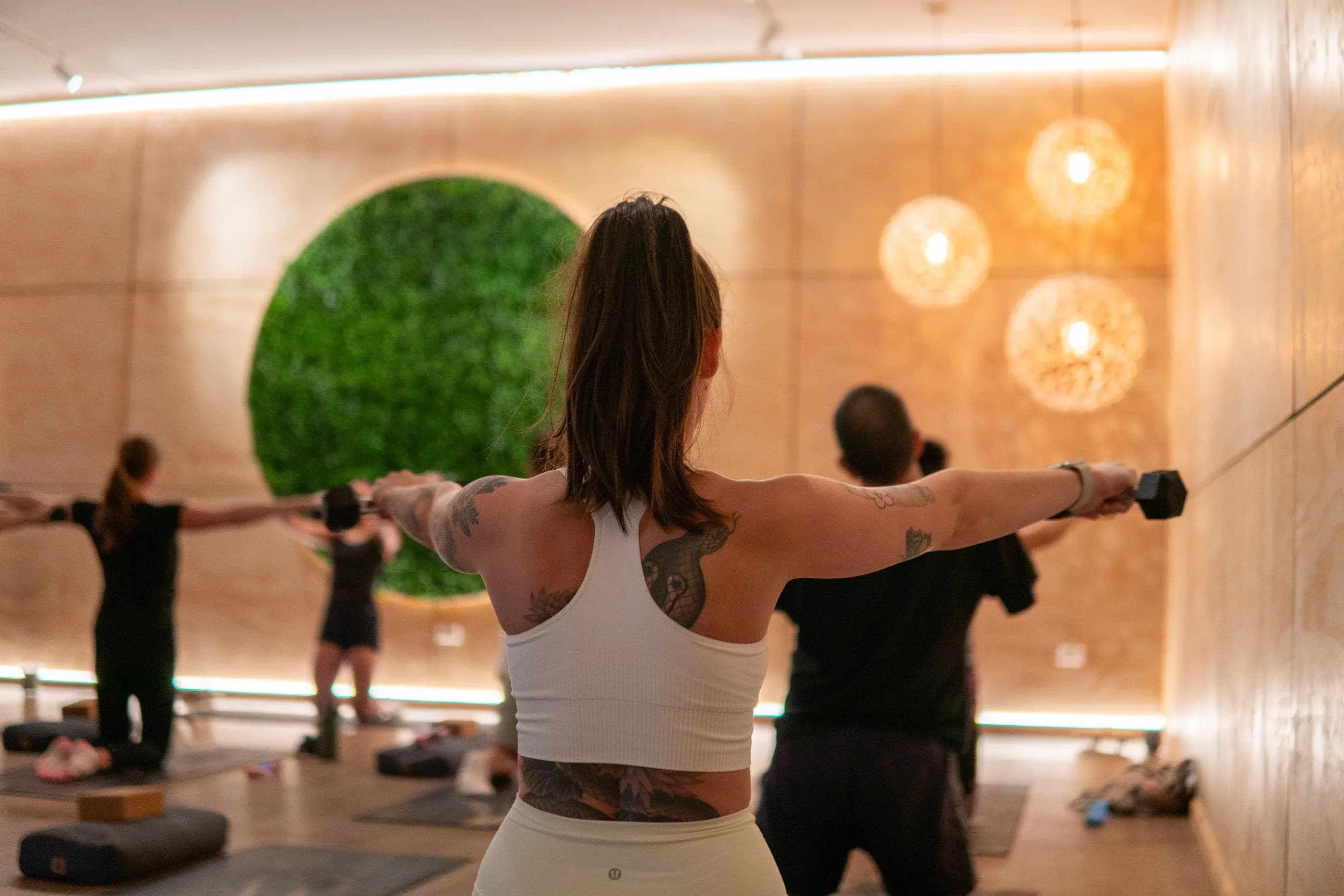 A member lifting dumbbells in front of the green foliage circle at Fit Nation Mount Maunganui